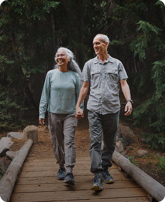 smiling senior couple hiking across forest bridge