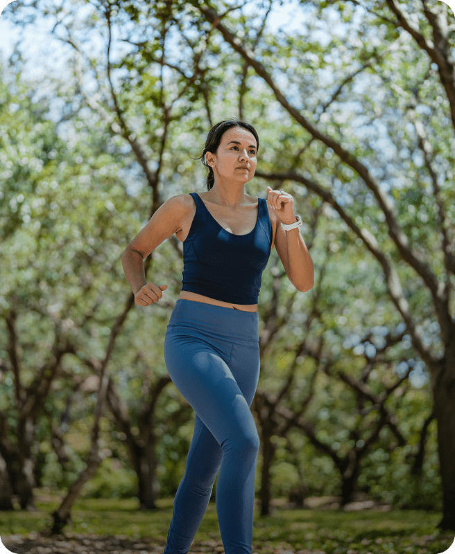 Woman jogging through a sunny forest path.