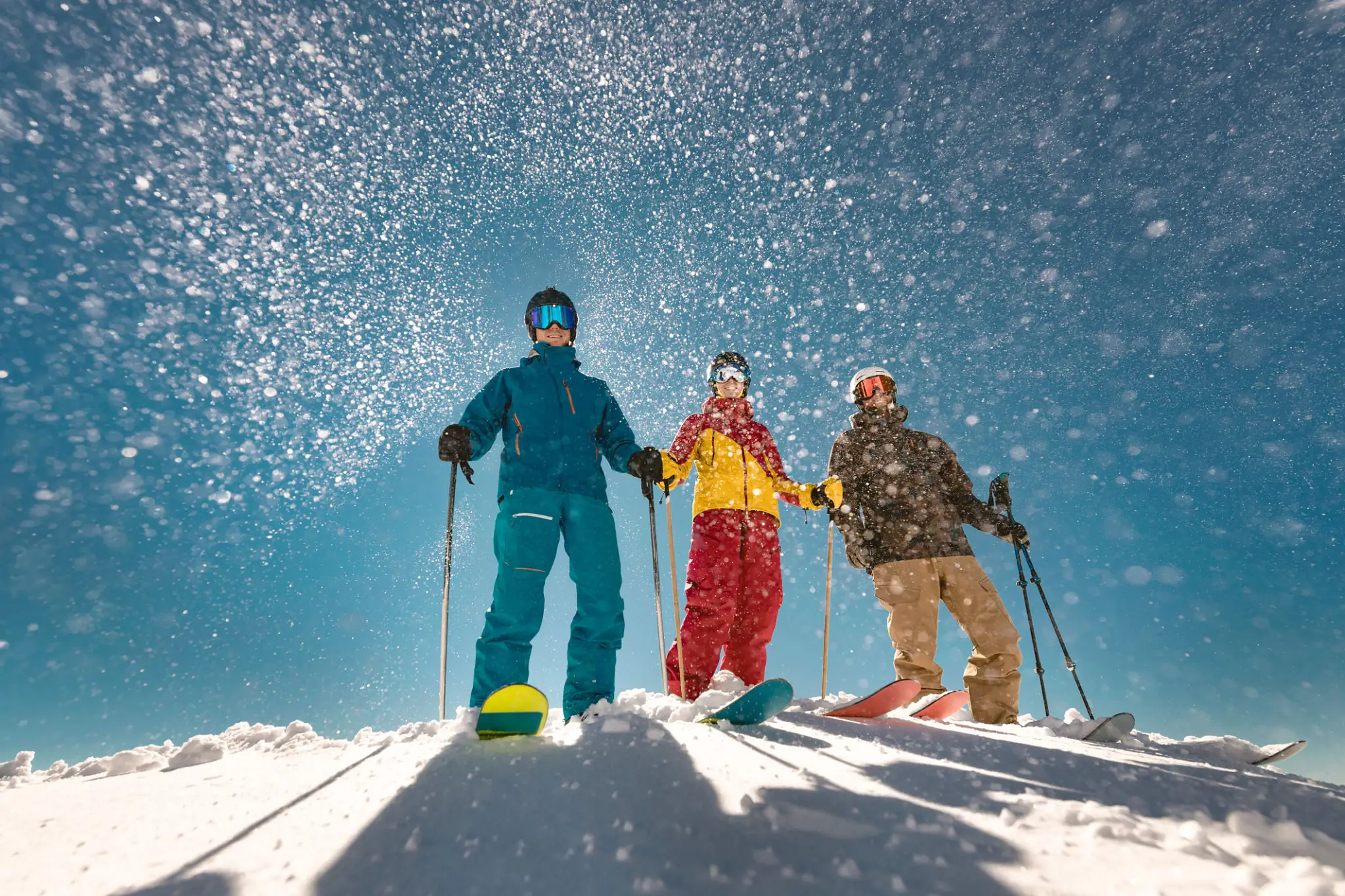Three skiers on sunny snowy slope, blue sky